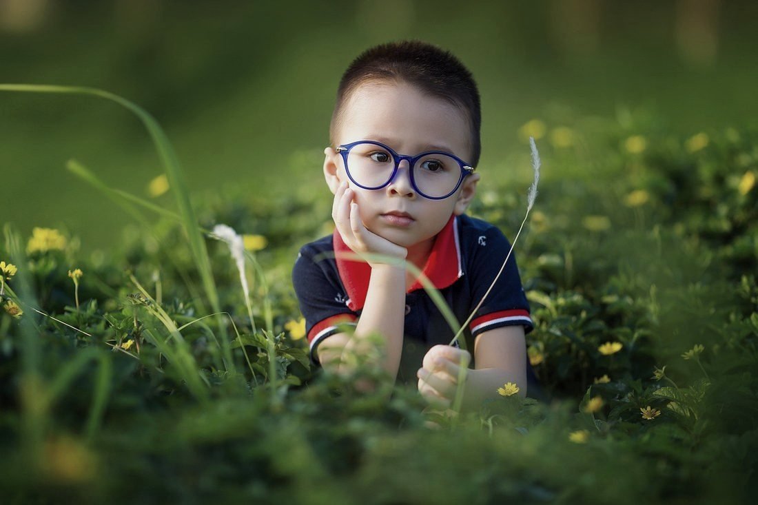 A child wearing round prescription glasses outdoors.